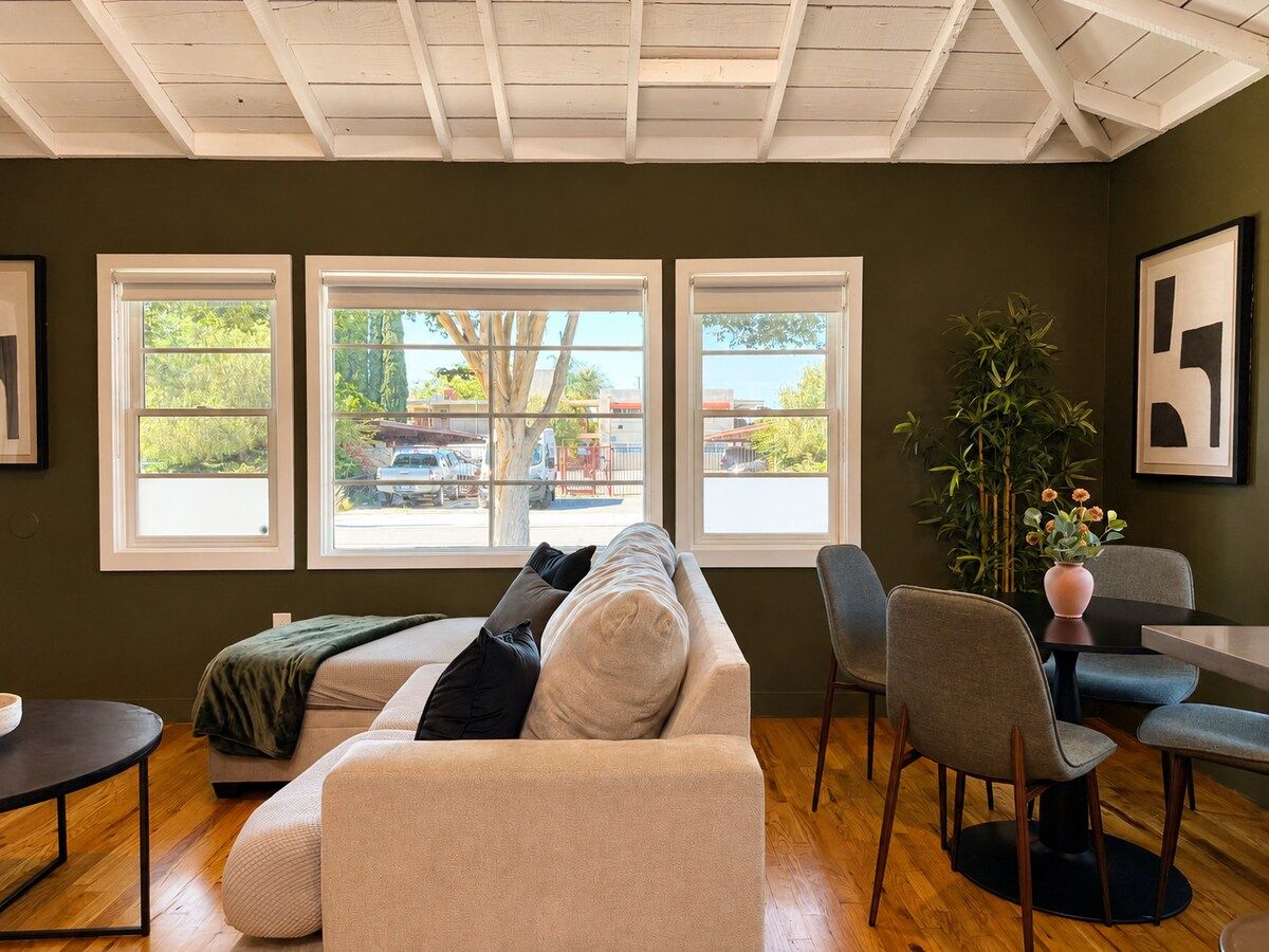 A living room with a sofa, chairs, a table, and large windows with a view of the outside.