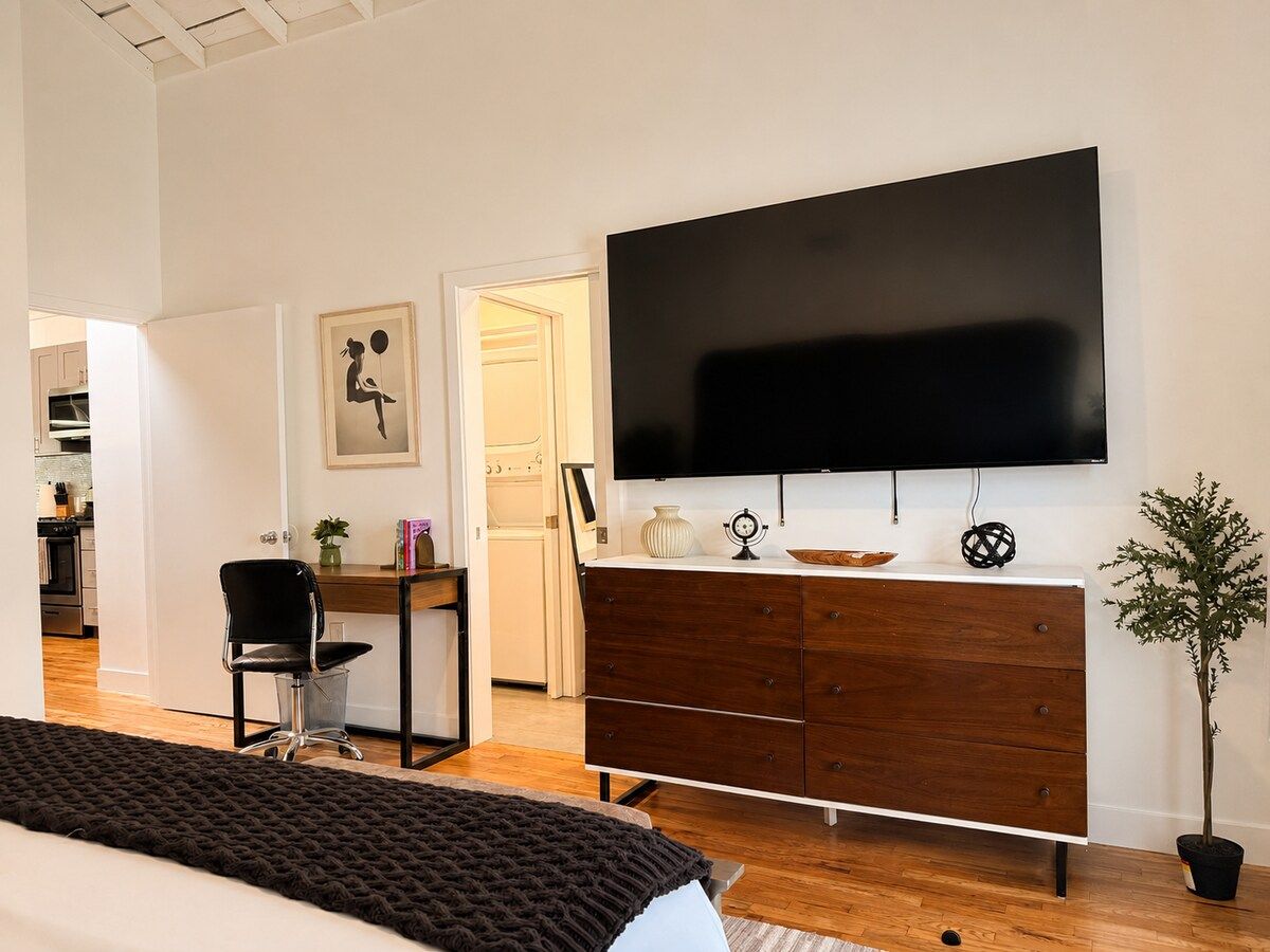 A modern bedroom with a bed, a dresser, a desk, and a television.