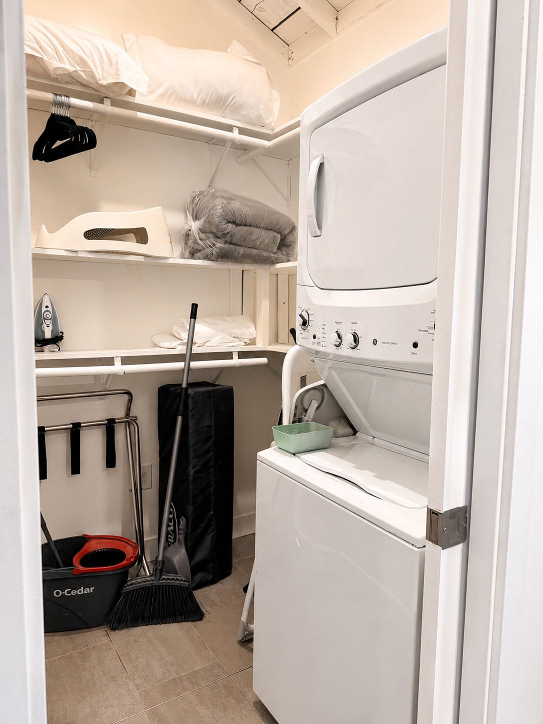 A laundry room with a washing machine, ironing board, and storage shelves.