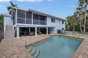 Ein zweistöckiges Haus mit Swimmingpool, Gartenmöbeln und einer überdachten Terrasse.