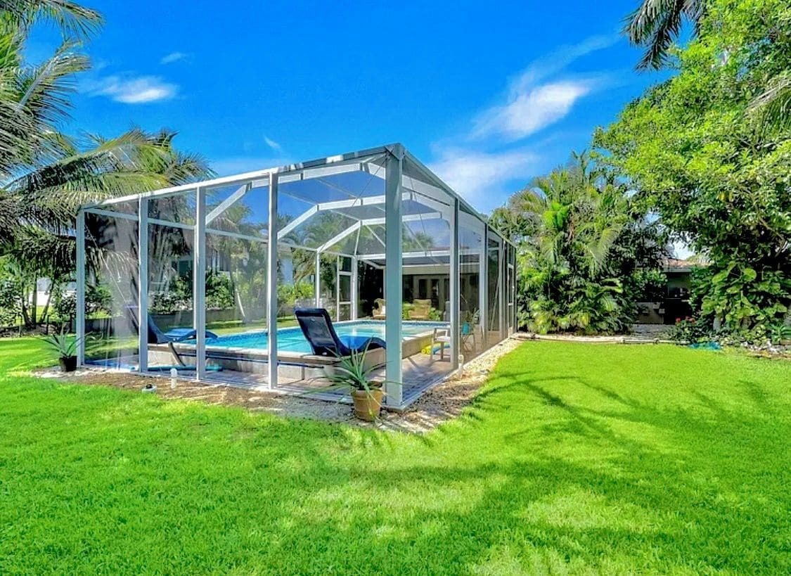 A glass-enclosed pool area with a clear sky, surrounded by lush greenery.
