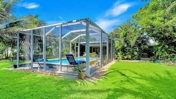 A glass-enclosed pool area with a clear sky, surrounded by lush greenery.
