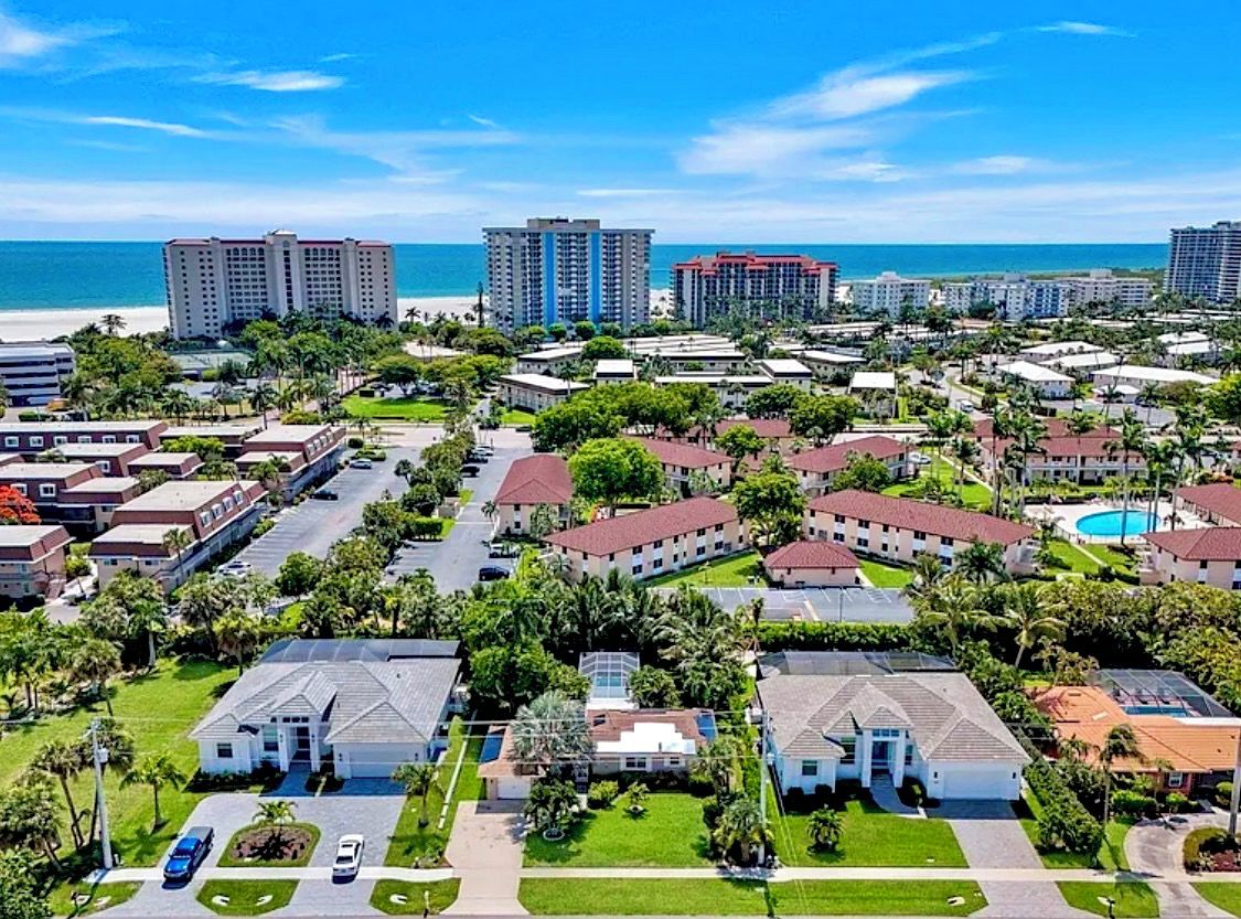 A coastal residential area with multiple-story buildings, a beach, and a clear sky.