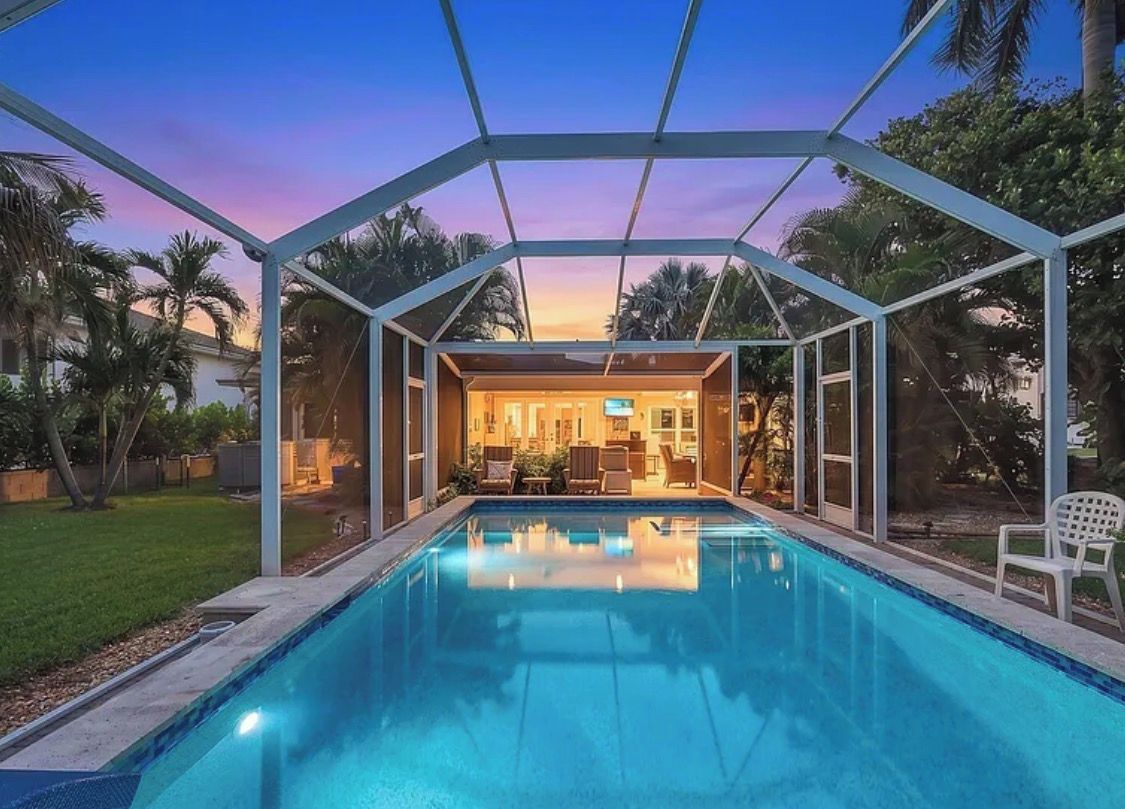 A swimming pool with a covered area, surrounded by palm trees and a sunset view.