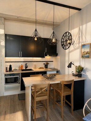 A modern kitchen with black cabinets, a wooden dining table, and pendant lights. - Le Passage du Colbert - Comfort & Design - Downtown (Tours)