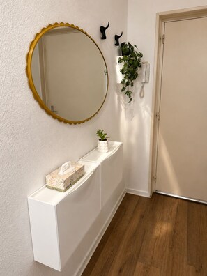 A hallway with a white console table, a round mirror with a gold frame, a potted plant, and a telephone. - Le Passage du Colbert - Comfort & Design - Downtown (Tours)