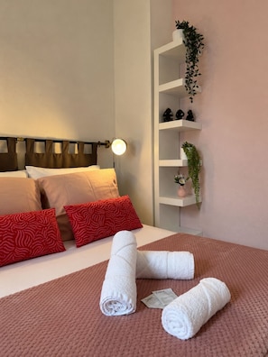 A neatly made bed with white and red pillows, a bedside lamp, and a wall-mounted shelf with decorative items and plants. - Le Passage du Colbert - Comfort & Design - Downtown (Tours)