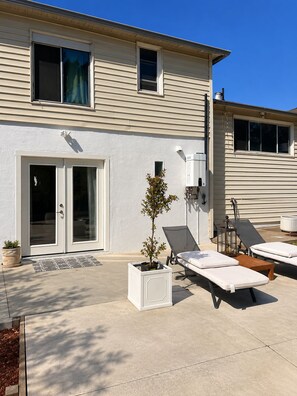 A two-story building with a patio area featuring a small tree, outdoor seating, and a sliding glass door entrance. - Serene studio apartment in beautiful Daly City perfect for relaxing (Daly City)