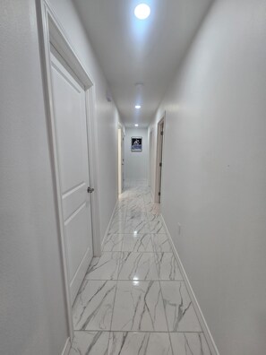 Un corridoio con pareti bianche, pavimento in marmo e una luce a soffitto.