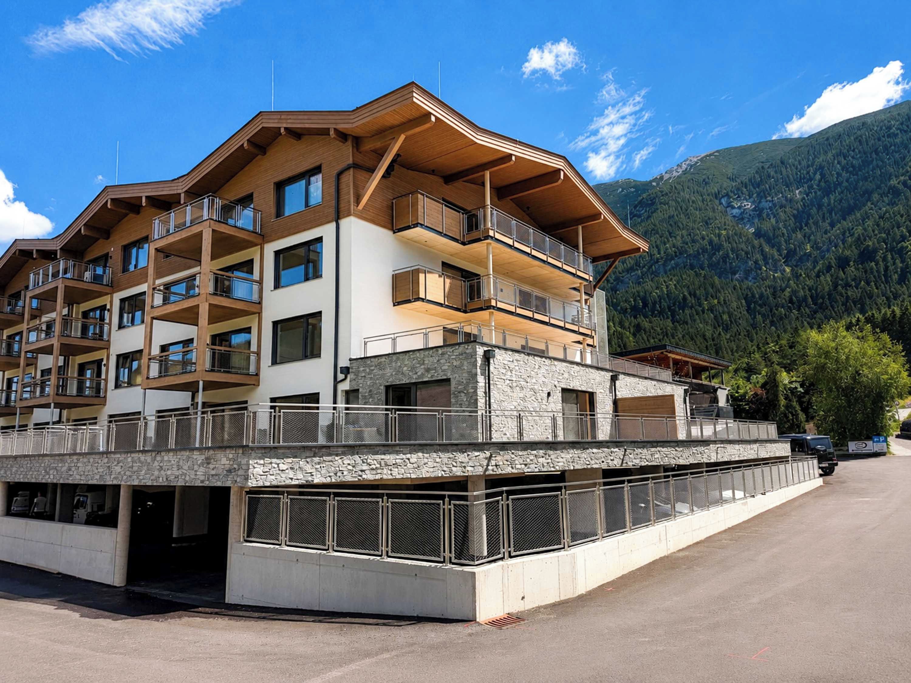 Ein mehrstöckiges Hotel mit Balkonen, einer Steinaußenfassade und einer Bergkulisse im Hintergrund.
