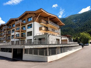 Ein mehrstöckiges Hotel mit Balkonen, einer Steinaußenfassade und einer Bergkulisse im Hintergrund.