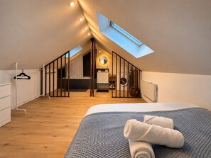 A bedroom with a skylight, wooden flooring, a bed with a grey textured blanket, and a hanging garment rack. - The Duplex des Prébendes - Central (Tours)