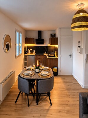 A compact kitchen with a dining area, featuring a round table set for four, a built-in oven, and a hanging light fixture. - The Duplex des Prébendes - Central (Tours)