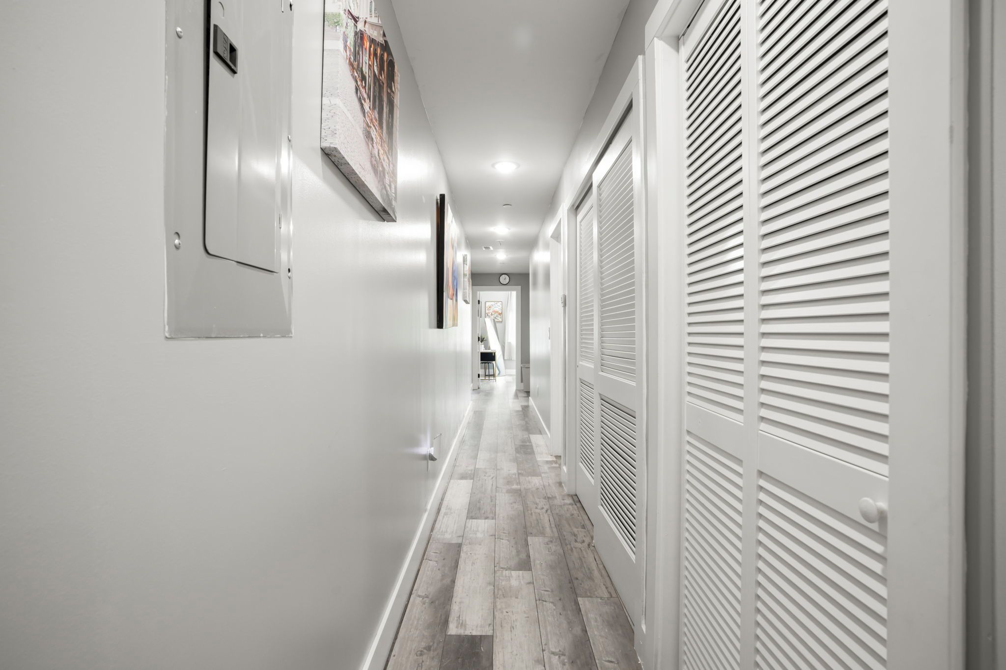 A hallway with a wooden floor, white walls, and a door with a window.