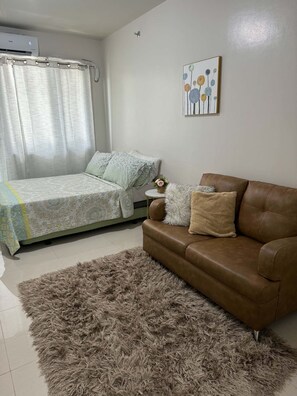 Ein Schlafzimmer mit einem Bett, einem braunen Ledersofa, einem flauschigen Teppich und einer Wand-Klimaanlage.