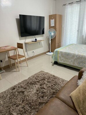 Ein Schlafzimmer mit Bett, Schreibtisch, Stuhl, Fernseher, Kleiderschrank und Stehlampe.