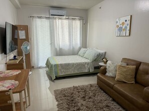 Ein Schlafzimmer mit einem Bett, einem braunen Sofa, einem Fernseher und einem Schreibtisch mit einem Ventilator.