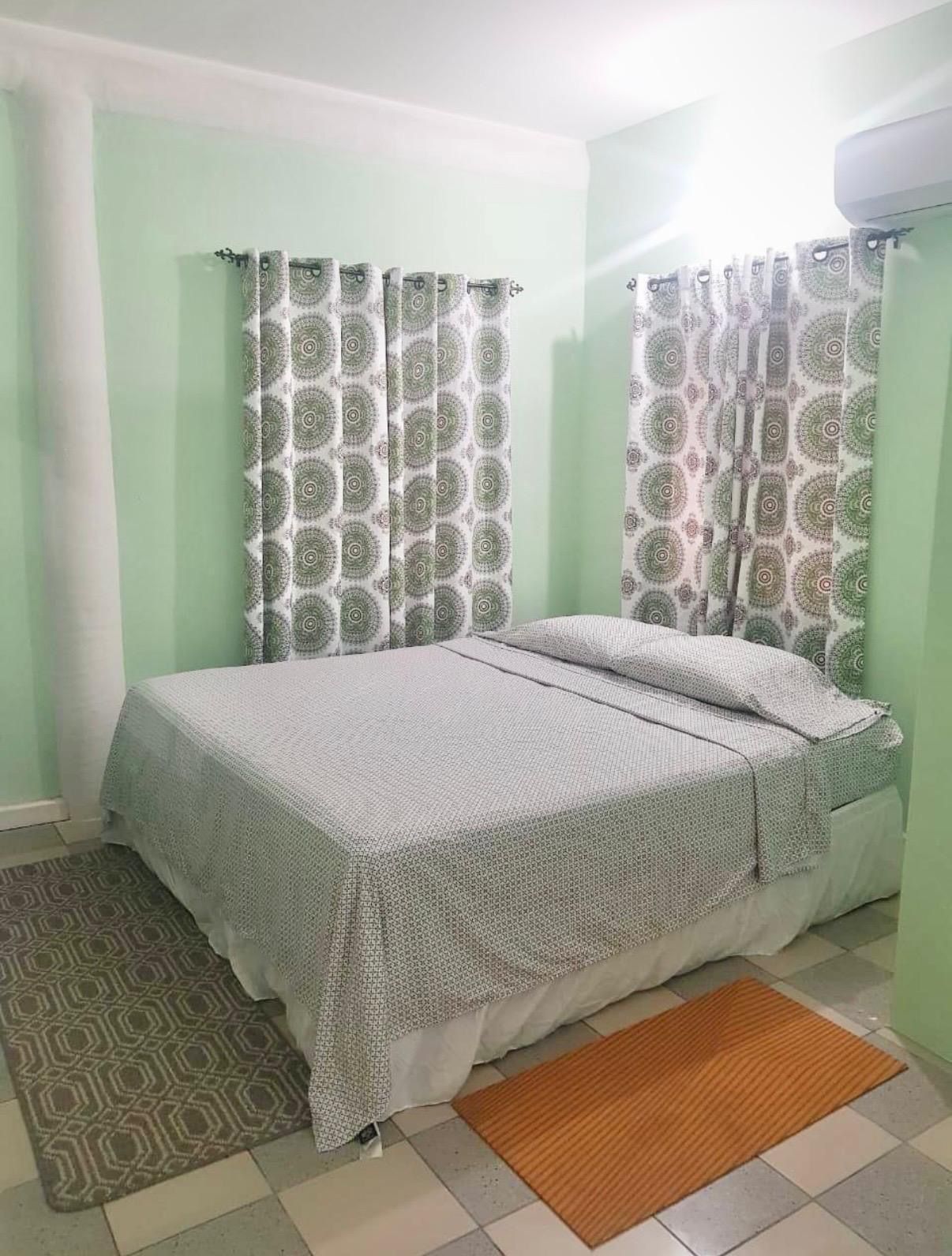 Une chambre à coucher avec un lit, des rideaux à motifs, un tapis à motifs et un mur de couleur claire.