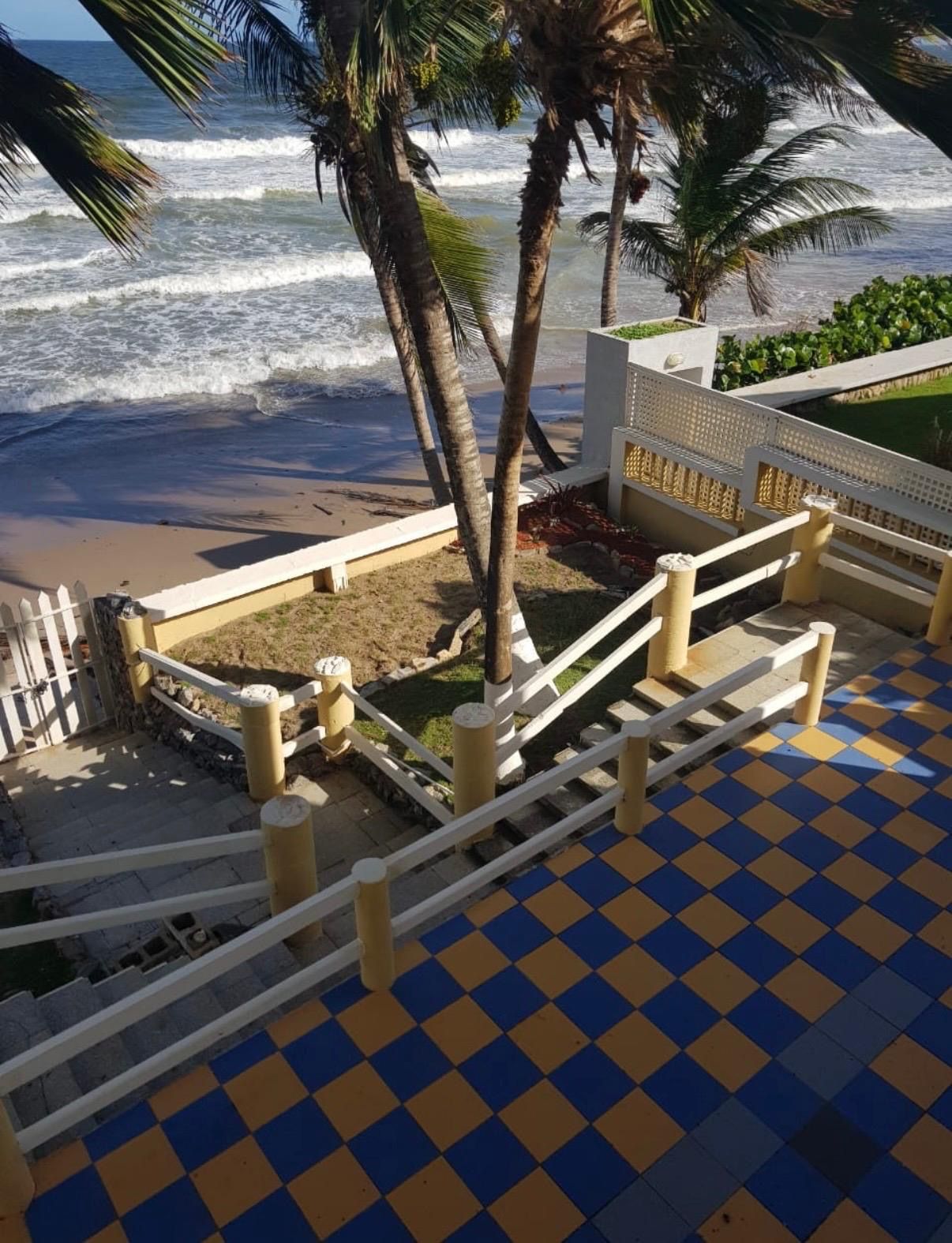 Un escalier menant à une plage bordée de palmiers et baignée par les vagues de l’océan.