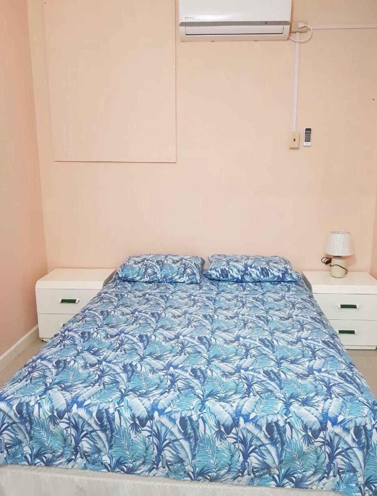 A bedroom with a bed, a nightstand, a lamp, and a wall-mounted air conditioner.