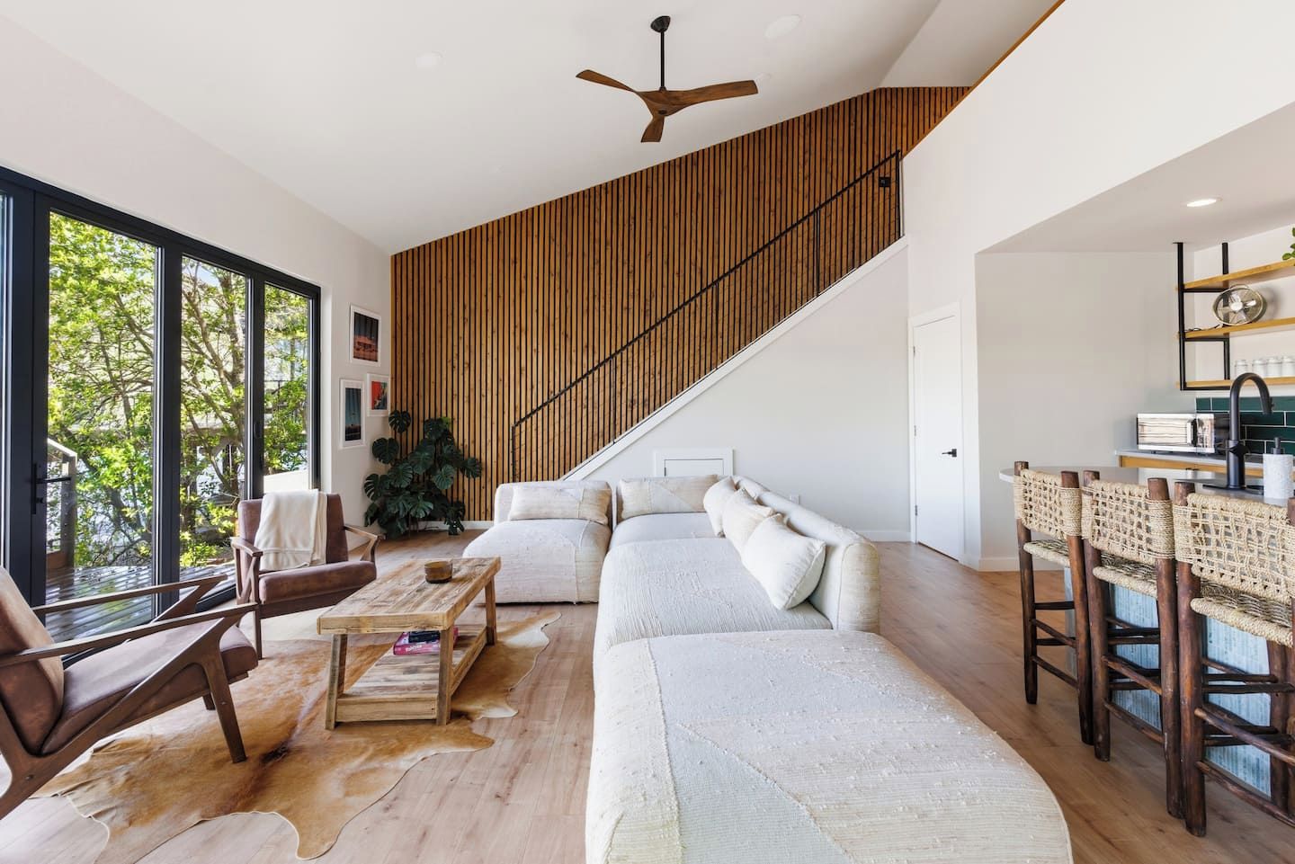A spacious living area with a large sofa, a wooden staircase, and a view of greenery outside.