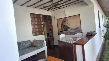 Een kamer met een houten plafond, een bank met gekleurde kussens, een schilderij van een leeuw en een klein tafeltje met een schaal.