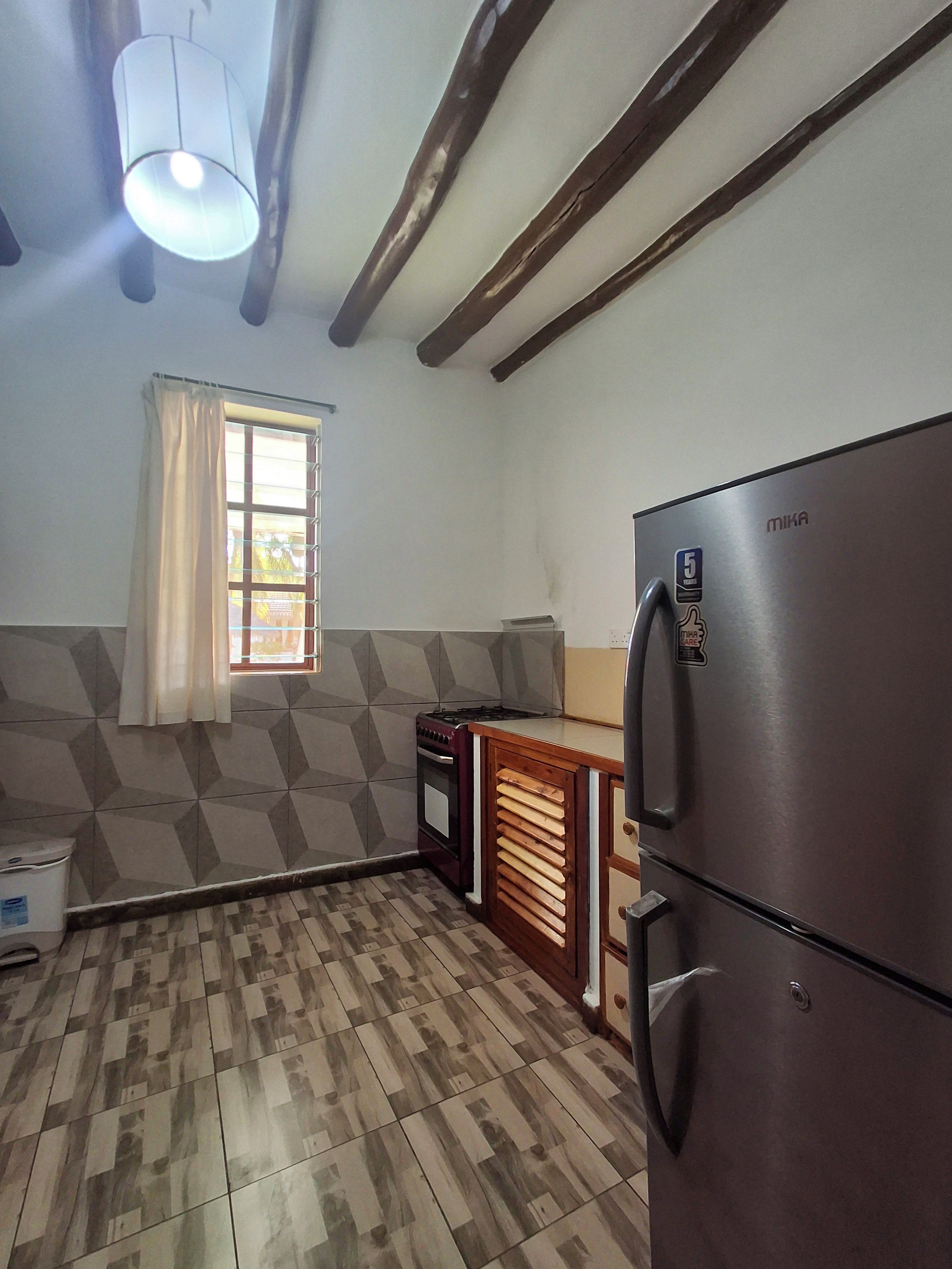 A kitchen with a built-in stove, a refrigerator, and a window with curtains.