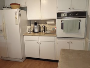 Une cuisine avec des meubles blancs, un réfrigérateur, une machine à café et un four.