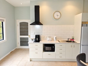 A modern kitchen with white cabinetry, a black range hood, a wall clock, a coffee maker, a toaster, a kettle, and a refrigerator.