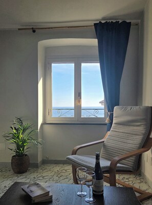A room with a view of the sea, a chair, a table with a bottle and glasses, and a potted plant. - BluOltremare Nervi - Historical Seaview Residence (Genova)