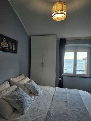 A bedroom with a bed, a wardrobe, a window with a view of the sea, and a hanging light fixture. - BluOltremare Nervi - Historical Seaview Residence (Genova)