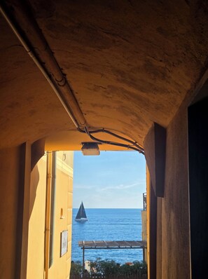 A view through an archway with a sailboat on the water and a building in the background. - BluOltremare Nervi - Historical Seaview Residence (Genova)