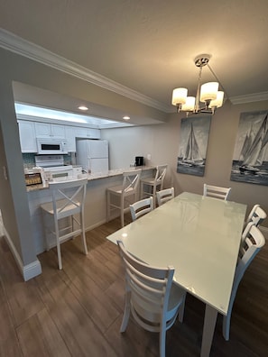 A modern kitchen with white cabinetry, a dining table with chairs, and a chandelier. - Sundial F203 Sanibel Beach Condo Steps to Beach (Sanibel)