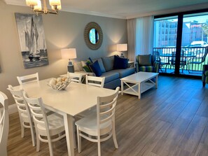 Sala de estar com área de jantar, um sofá, uma mesa de centro e vista através de uma porta de vidro.