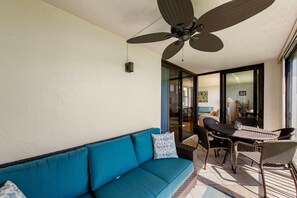 A sunlit room with a blue sofa, wicker chairs, and a ceiling fan. - Direct Gulf Beachfront Water Views East End (Sanibel)
