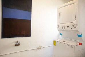 A laundry room with a washing machine, a wall-mounted drying rack, and a large abstract painting. - ⭐ Charming Bucerías Hacienda | Private Pool & Courtyard (Bucerías)