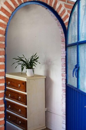 Ein Zimmer mit einem hölzernen Schminktisch, einer Topfpflanze und einer blauen Tür.