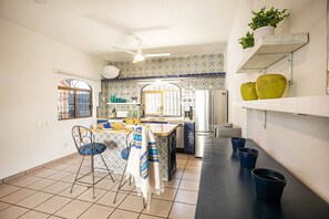 A kitchen with a tiled backsplash, a refrigerator, a coffee maker, and a dining area with chairs and a table. - ⭐ Charming Bucerías Hacienda | Private Pool & Courtyard (Bucerías)