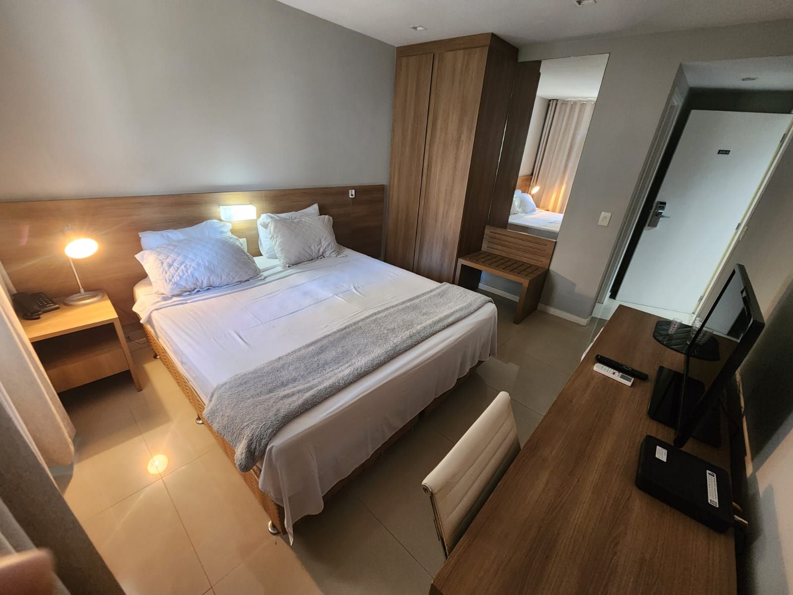 Ett hotellrum med en stor säng, sängbord, ett skrivbord, en stol, en TV och en garderob.