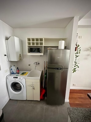 A compact kitchen with a washing machine, a refrigerator, a microwave, and a sink. - Confortable 3 Ambientes en Núñez, zona Segura, conectado y con Balcón (Buenos Aires)