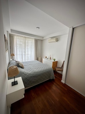 A bedroom with a bed, bedside table, lamp, chair, desk, and an air conditioning unit. - Confortable 3 Ambientes en Núñez, zona Segura, conectado y con Balcón (Buenos Aires)