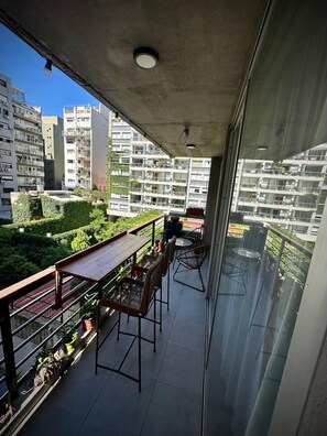 A balcony with a view of a residential area, featuring a wooden table and chairs, potted plants, and a metal railing. - Confortable 3 Ambientes en Núñez, zona Segura, conectado y con Balcón (Buenos Aires)