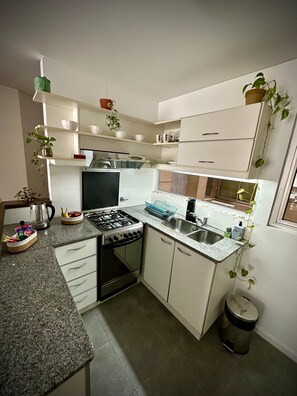 Una cucina funzionale con mobili bianchi, un fornello a gas, un lavello e un cestino.