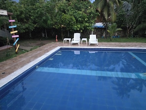 A swimming pool with a tiled edge, surrounded by white lounge chairs, and a signpost with multiple directional signs.