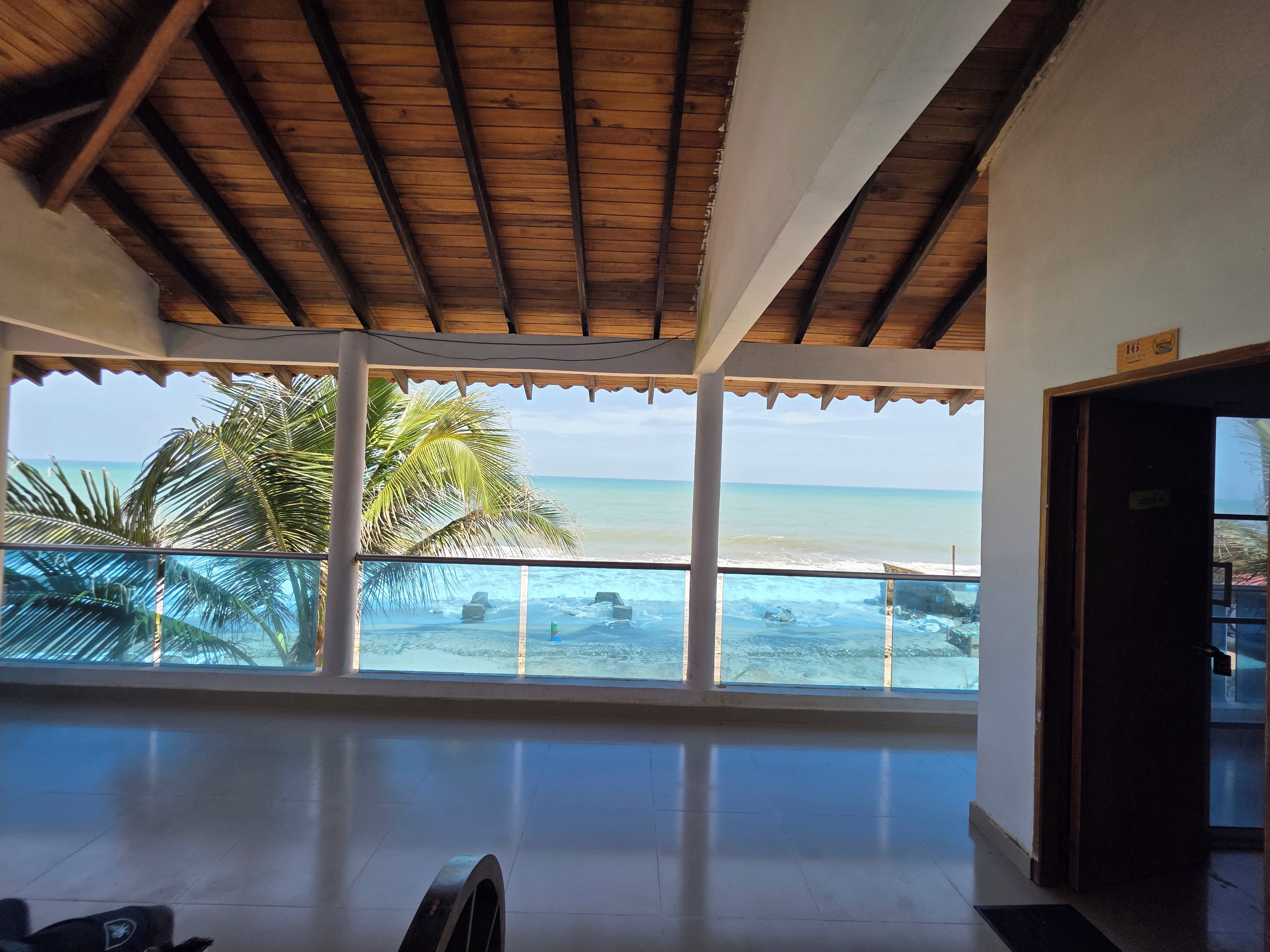 Una habitación con vistas al océano a través de amplios ventanales, suelo de baldosas y techo de madera.