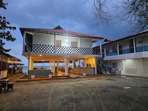 Um edifício de dois andares com varanda, área de estar coberta e vista para o mar.
