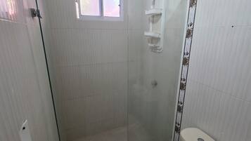 Casa de banho com cabine de duche em vidro, sanita e janela.