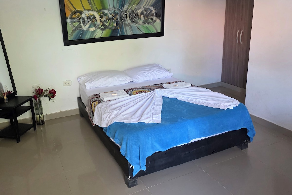 Quarto com cama, pintura na parede, guarda-roupa e uma pequena mesa com um vaso de flores.