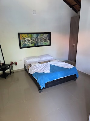 Quarto com cama, pintura na parede, guarda-roupa e uma pequena mesa com um vaso de flores.