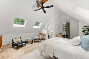 Ein Schlafzimmer mit schrägem Dach, einem Bett, einem Schreibtisch und zwei Fenstern.